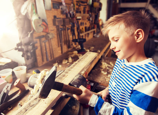 happy little boy with hammer and plank at workshop - Foto, Imagen