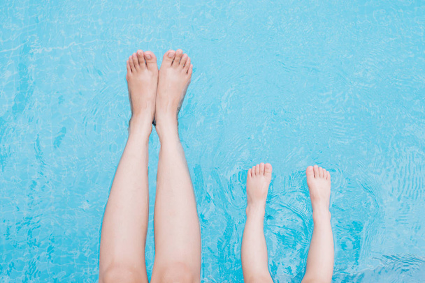Child and adult legs underwater in the swimming pool - Фото, изображение