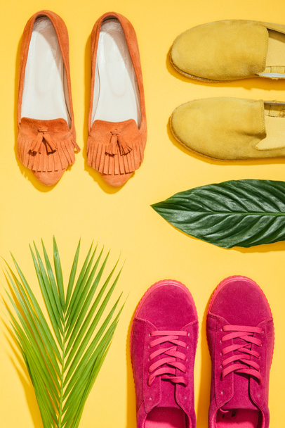 top view of tropical leaves and stylish female shoes on yellow background - Photo, Image