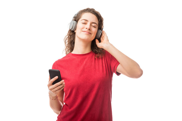 Όμορφη νεαρή γυναίκα που φοράει ακουστικά να ακούτε μουσική από το smartphone που απομονώνονται σε λευκό φόντο - Φωτογραφία, εικόνα