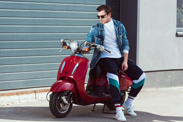 handsome young man in stylish vintage clothes sitting on scooter - 写真・画像