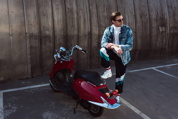 красивый молодой человек в стильной джинсовой куртке с винтажным скутером на парковке
 - Фото, изображение