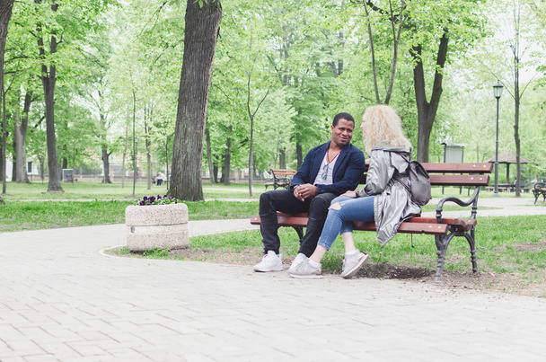 Multiracial young couple sitting on bench in park - Foto, Bild