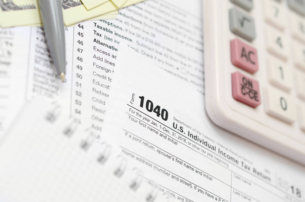 Ручка, ноутбук, калькулятор, и долларовые купюры лежит на налоговой форме 1040 США Индивидуальная налоговая декларация. Время платить налоги
 - Фото, изображение