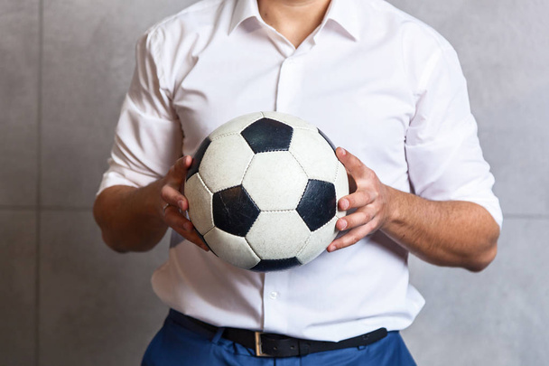 A businessman in a white shirt is standing near the wall and holding a soccer ball in his hands. - 写真・画像