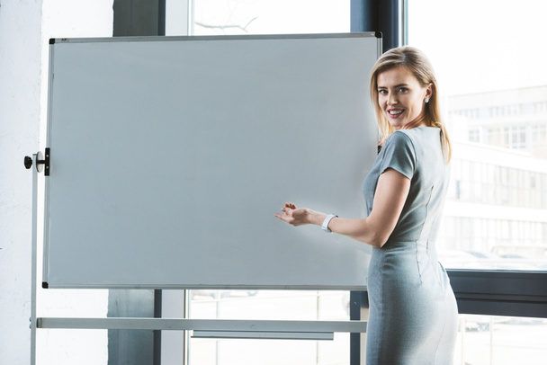 businesswoman pointing at blank whiteboard and smiling at camera - 写真・画像