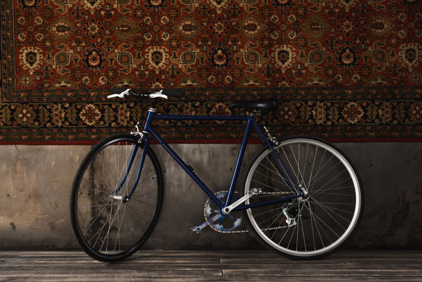 вінтажний дорожній велосипед в приміщенні перед килимком, що звисає на стіні
 - Фото, зображення