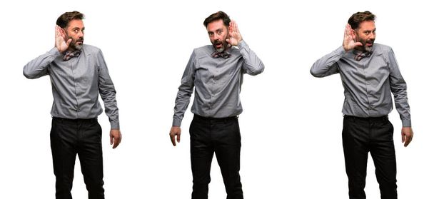 Μέση ηλικία άνθρωπος, με γενειάδα και παπιγιόν, κρατώντας το χέρι κοντά στο αυτί που προσπαθεί να Ακούστε ενδιαφέρουσες ειδήσεις εκφράζοντας την έννοια επικοινωνίας και κουτσομπολιό - Φωτογραφία, εικόνα