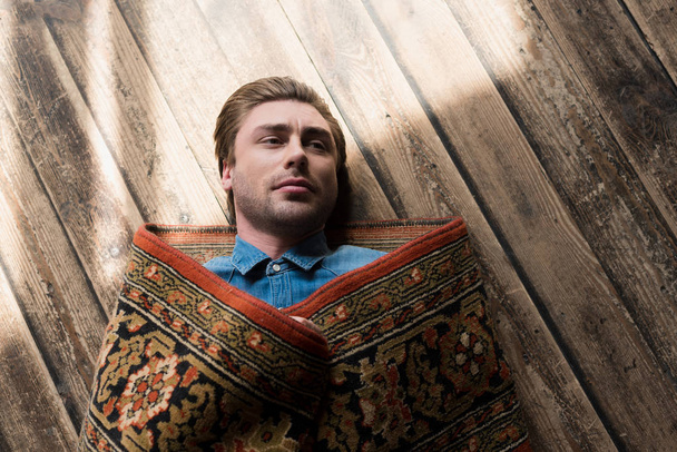 top view of handsome young man covered in rug lying on wooden floor - Photo, Image