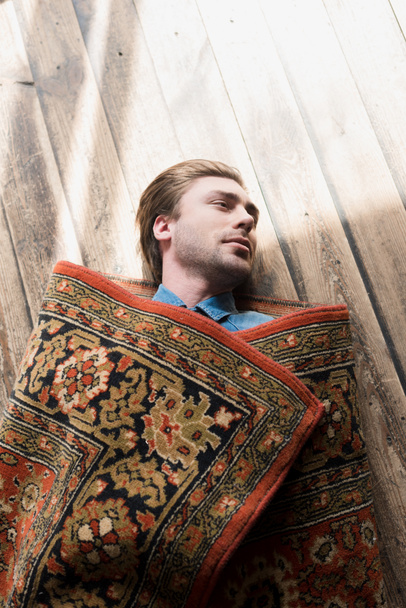 木製の床の上に横たわる敷物で覆われている若い男のトップ ビュー - 写真・画像