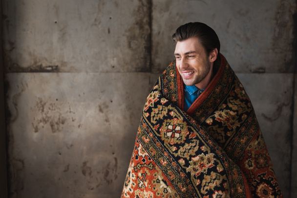 χαρούμενος νεαρός άνδρας που καλύπτονται σε κουβέρτα μπροστά από το τσιμεντένιο τοίχο - Φωτογραφία, εικόνα