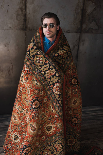 stylish young man covered in rug in front of concrete wall - Zdjęcie, obraz