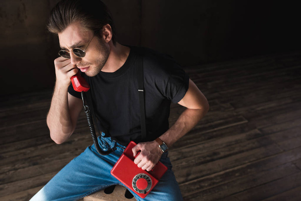 vysoký úhel pohled pohledný mladý muž v černé tričko a šle mluví o retro kabelové červený telefon - Fotografie, Obrázek