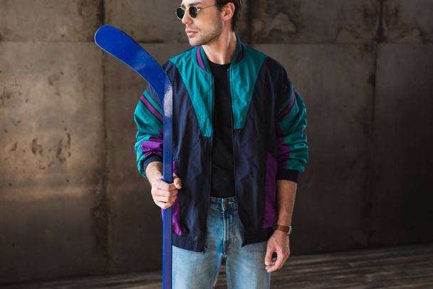 stylish young man in vintage windcheater and sunglasses with hockey stick looking away - Foto, Imagem