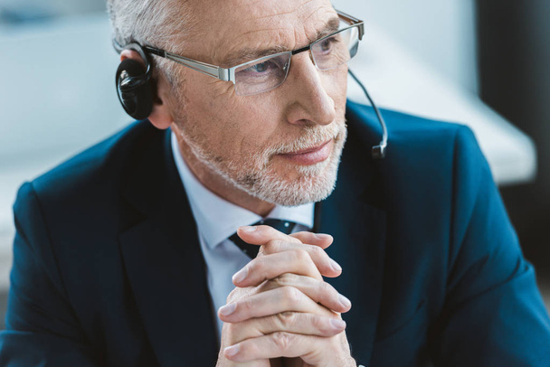 close-up portrait of senior businessman in eyeglasses and headset looking away - Foto, Bild