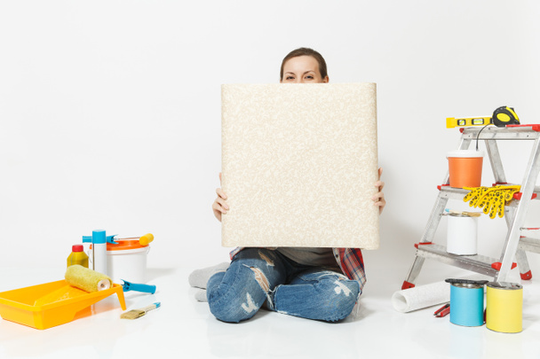 Woman in casual clothes sitting on floor with unfolded roll of wallpaper instruments for renovation apartment isolated on white background. Accessories for gluing tools. Repair home concept Copy space - Photo, Image