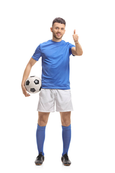 Full length portrait of a soccer player holding a football and making a thumb up sign isolated on white background - Foto, Imagem