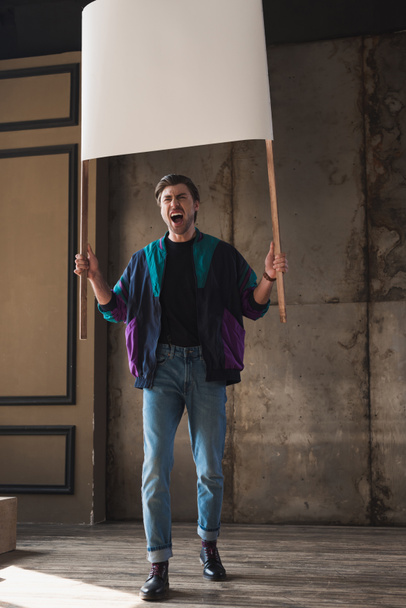 angry shouting young man in vintage windcheater with blank placard - Foto, afbeelding