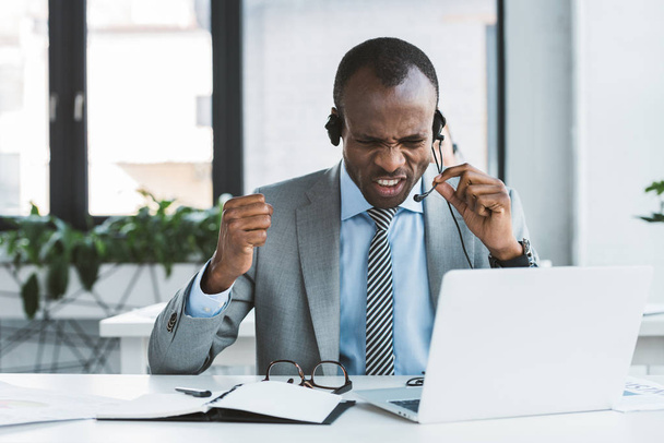 empresario afroamericano emocional gritándole a los auriculares en el lugar de trabajo
 - Foto, imagen