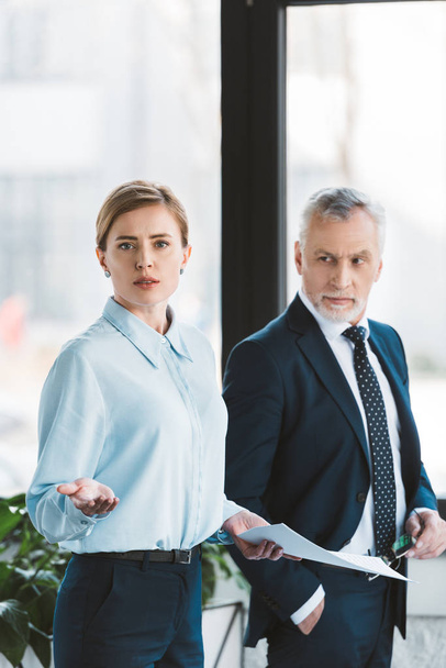 senior businessman looking at businesswoman holding papers and looking at camera - Фото, изображение