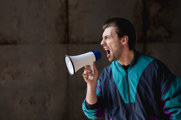 side view of angry young man in vintage windcheater shouting with loudspeaker - Fotografie, Obrázek