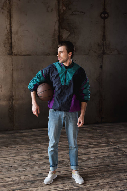 attractive young man in vintage windcheater with basketball ball looking away - Fotó, kép
