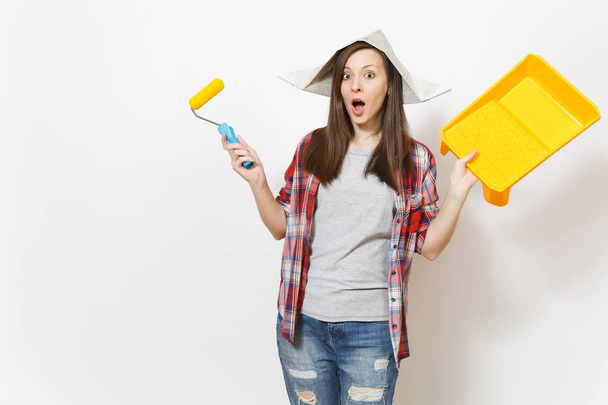 Young shocked beautiful woman in newspaper hat holding roller for wall painting and paint tray isolated on white background. Instruments, tools for renovation apartment room. Repair home concept. - Фото, зображення