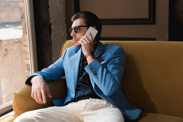 stylish young man talking by phone while sitting on couch - Фото, зображення