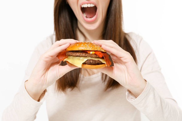 Bliska przycięte strzał młoda kobieta, trzymając w rękach burger, stara się jeść na białym tle na białym tle. Prawidłowe odżywianie lub klasyczny amerykański fast food. Kopiować miejsca na ogłoszenie. Powierzchnia reklamowa. - Zdjęcie, obraz