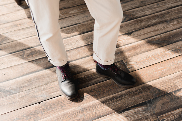 обрезанный снимок человека в стильной обуви и брюках, стоящих на деревенском деревянном полу
 - Фото, изображение