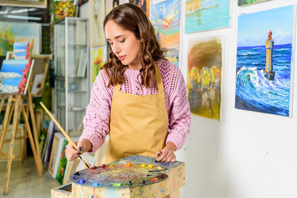 beautiful female artist applying paints on palette in workshop - 写真・画像