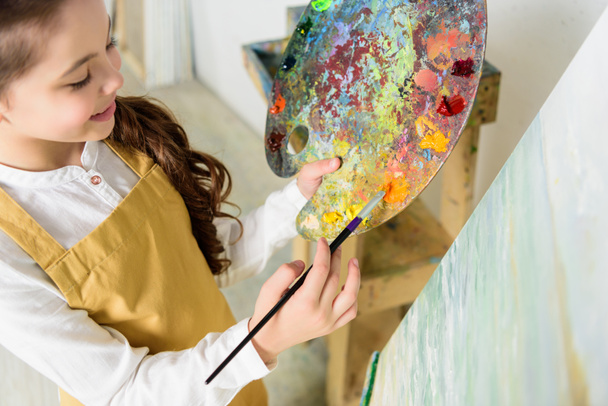 vista de ángulo alto del niño tomando pintura de la paleta en el taller de la escuela de arte
 - Foto, imagen