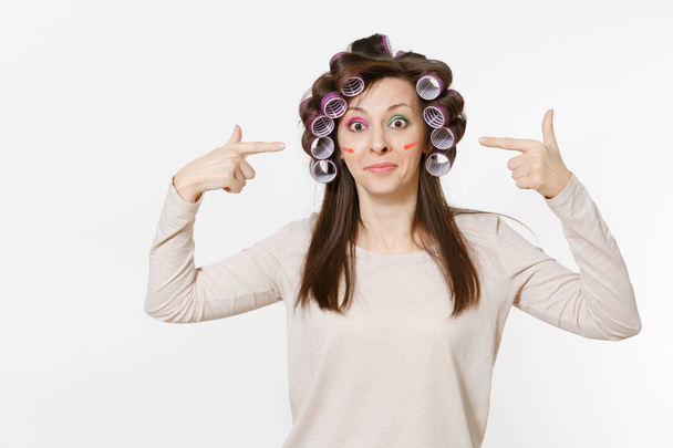 Fun young woman with curlers on hair standing isolated on white background. Crazy makeup with set facial decorative cosmetics. Beauty female fashion lifestyle concept. Advertisement area to copy space - Foto, imagen