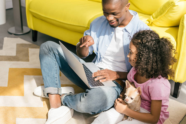 afroamericano padre y pequeña hija con perro usando portátil juntos en casa
 - Foto, Imagen