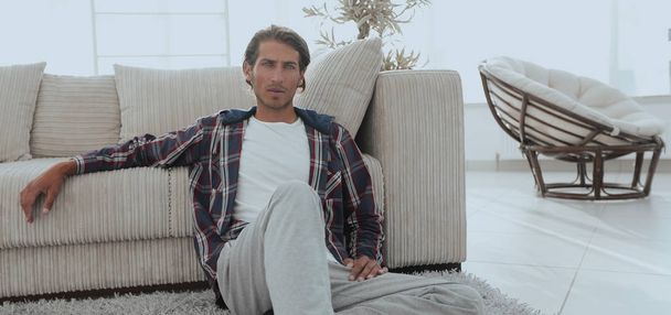 confident guy sitting on the carpet in a cozy living room. - Photo, Image