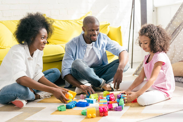 smiling african american family playing with colorful blocks together on floor at home - Photo, Image