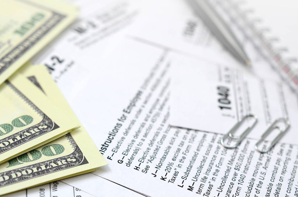 El bolígrafo, cuaderno y billetes de dólar se encuentra en el formulario de impuestos 1040 EE.UU. Declaración individual del impuesto sobre la renta. El momento de pagar impuestos
 - Foto, imagen