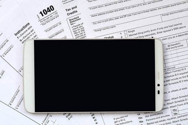Smartfona znajduje się formularz podatkowy 1040 i formularz w-2. Czysty czarny ekran smartphone do umieszczenia tekstu - Zdjęcie, obraz