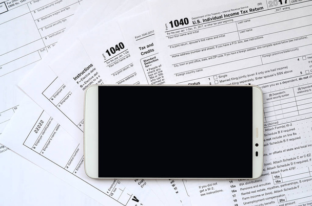 De smartphone ligt op de belastingformulier 1040 en W-2. Schoon zwart scherm smartphone voor plaatsing van de tekst - Foto, afbeelding