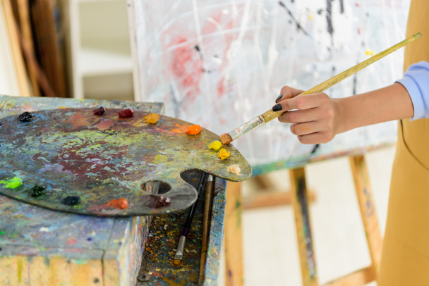 cropped image of left-handed artist taking paint from palette in workshop - Fotó, kép