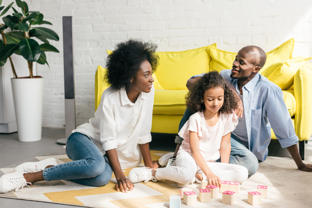 afrikanisch-amerikanische Eltern und Tochter spielen zu Hause gemeinsam mit Holzklötzen auf dem Boden - Foto, Bild