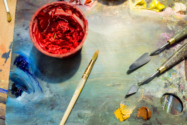 pinceles para pintar, paleta y pintura con póster rojo sobre mesa de madera en taller
 - Foto, Imagen
