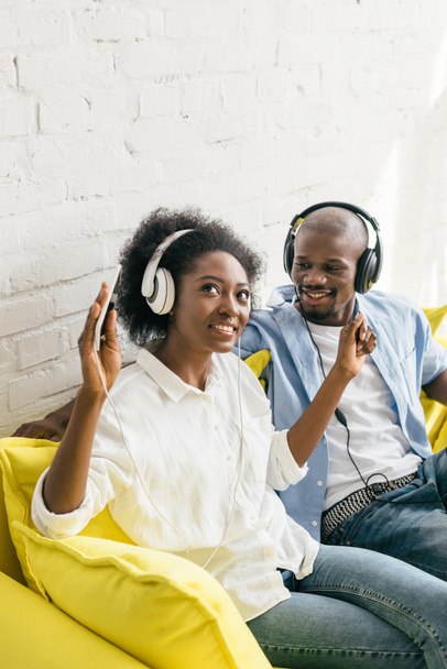 african american listening music in headphones while resting on sofa at home - Photo, Image