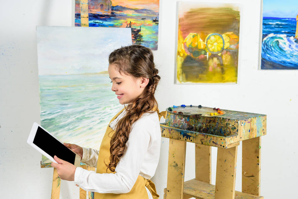 vista lateral del niño mirando la tableta en el taller de la escuela de arte
 - Foto, Imagen