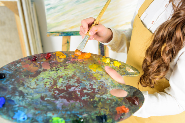 cropped image of child taking oil paints from palette in workshop of art school - Photo, Image