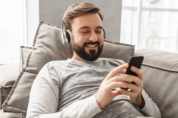 Happy relaxed guy 30s in basic clothing lying on sofa, and liste - 写真・画像