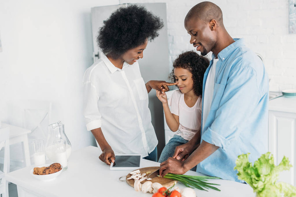 african american man cutting fresh vegetables for breakfast with family standing near by in kitchen at home - Valokuva, kuva