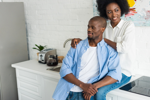 portrait of happy african american woman hugging husband in kitchen at home - Photo, Image