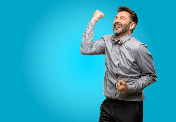 Мужчина средних лет, с бородой и галстуком-бабочкой счастлив и взволнован празднованием победы, выражая большой успех, силу, энергию и положительные эмоции. Празднует новую работу радостно
 - Фото, изображение