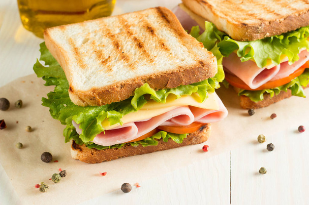 Close-up photo of a club sandwich. Sandwich with meet, prosciutto, salami, salad, vegetables, lettuce, tomato, onion and mustard on a fresh sliced rye bread on wooden background. Olives background. - Photo, Image
